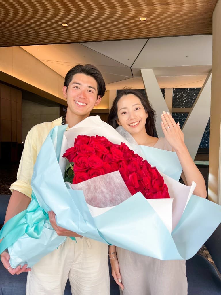 大きな赤いバラの花束を抱えて微笑むカップル
